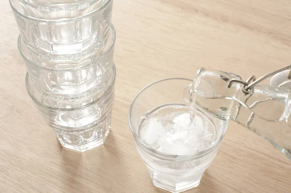 Pouring a glass of fresh pure water from a glass bottle into a tumbler containing ice for a healthy refreshing drink