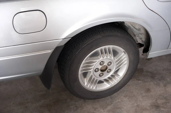 Looking Down at Wheel of Silver Car Showing Detail of Tire and Rim and Door for Gas Tank