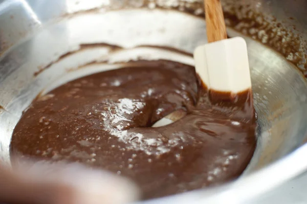 Cook making a bowl of chocolate icing cleaning around the edge of the mixing bowl with a rubber spatula