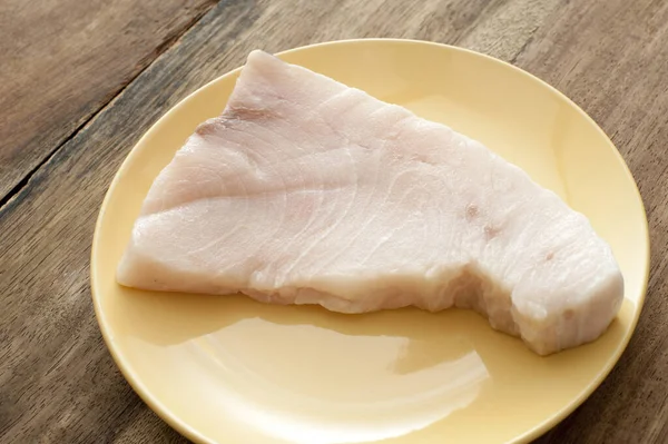 First person perspective view on large piece of raw swordfish in middle of yellow circular plate over dark wooden table