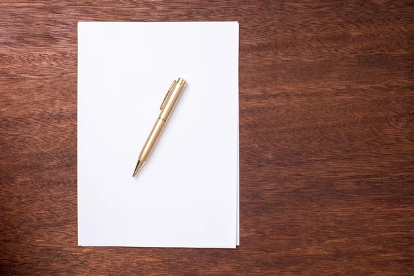 Concept of writers block with blank white page of paper with a ballpoint pen on top lying on a desk viewed from above