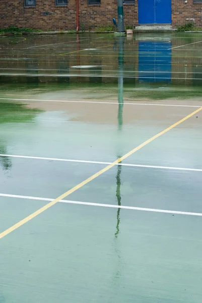Wet green surface of an all-weather sports court with reflections of the poles and painted lines in an urban or school environment