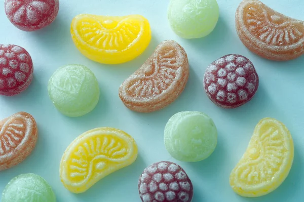 Lemon, lime, orange and raspberry shaped flavored candy pieces spaced out over green background