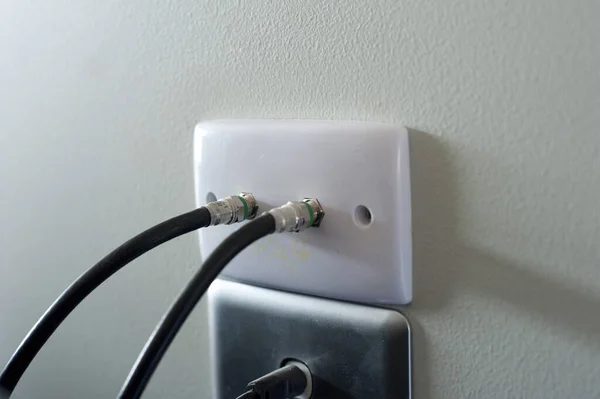 Wall socket with TV cables for comunication and broadcasting of the signal on a light grey interior wall, close up at an oblique angle