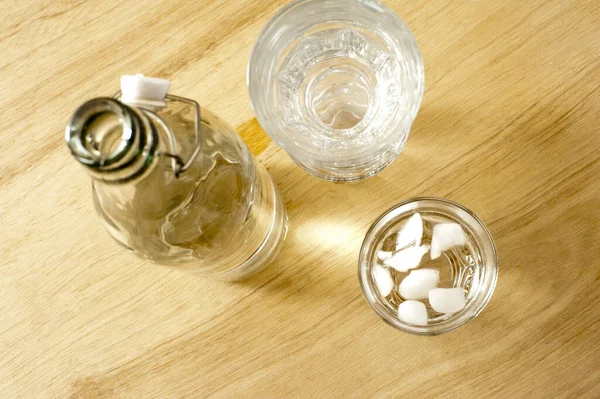 Iced water dispensed into a tumbler from a glass bottle with a resealable cap, view from above on a wooden table in a healthy drink and diet concept