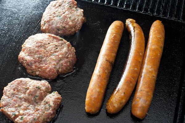 Beef patties and sausages grilling over the heat on a griddle on a barbecue, viewed from above