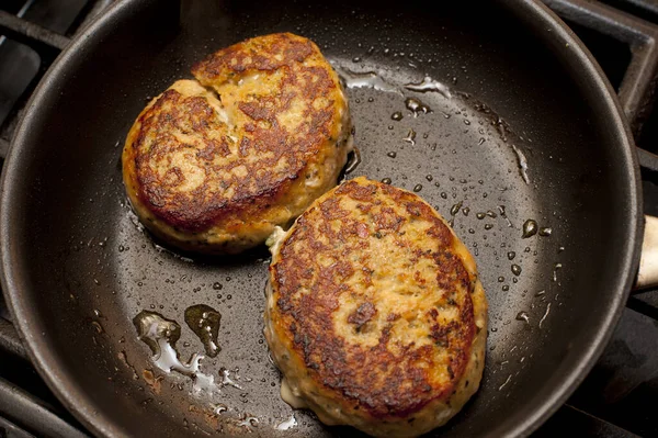 Pair of delicious cooked crab cakes frying in non-stick pan with drops of oil bubbling