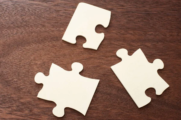 Close up of three blank jigsaw puzzle pieces placed in a triangle shape on a wood table