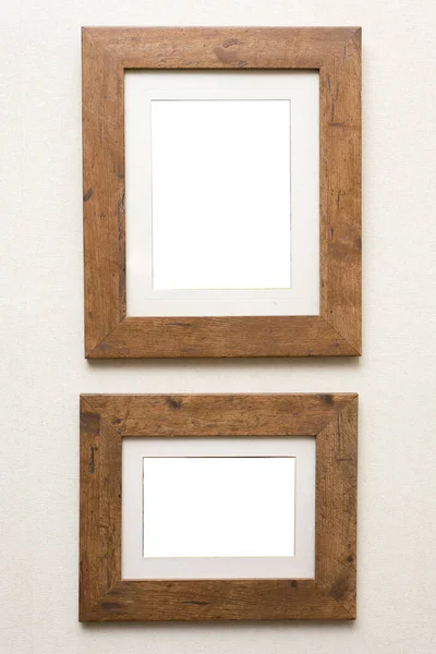 Two empty rustic wooden frames with neutral mount card inserts hanging on an off white wall ready for your artwork of photo