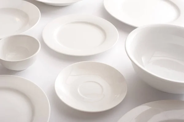 Assorted clean white plates, saucers and bowls laid out on a white table in a close up view