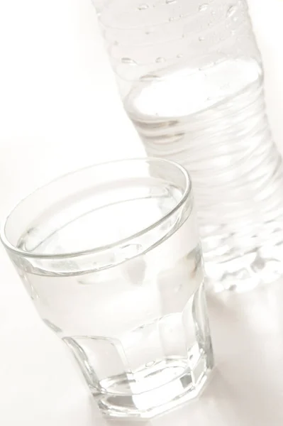 Glass of clear clean pure bottled water with the plastic bottle behind on a white background, close up tilted angle