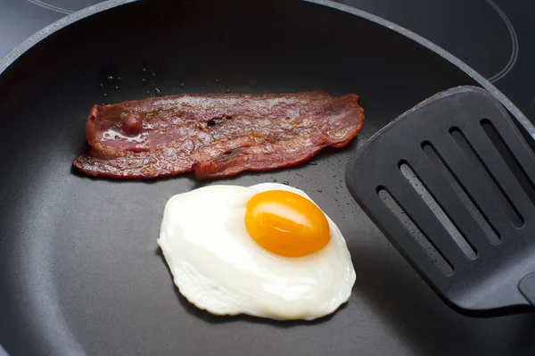 Frying an egg and crispy rasher of bacon for breakfast in a non-stick frying pan