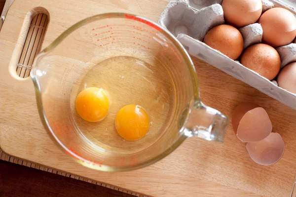 Overhead view of two cracked eggs with lovely yellow yolks in a glass measuring jug on a kitchen counter ready to be used as a baking ingredient