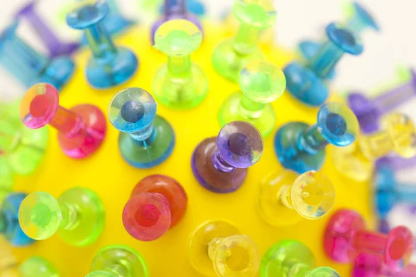 Purple, green, blue, pink and yellow plastic push pins stuck into round yellow ball