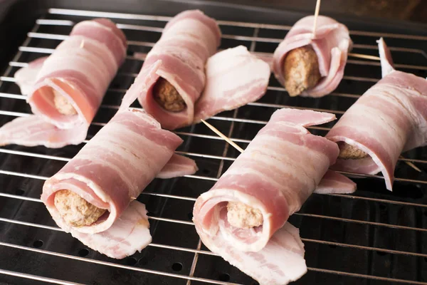 Uncooked Pigs in Blankets or Bacon Rolls with rashers of bacon wrapped around pork sausages ready for cooking on a grill pan