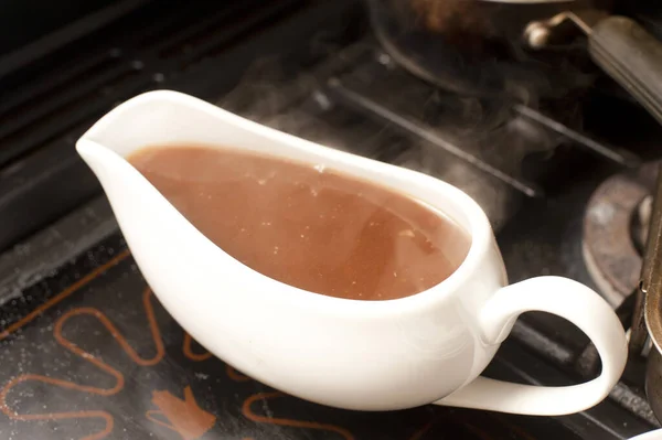 Gravy boat filled with rich hot gravy made from meat drippings and stock standing on a warming plate