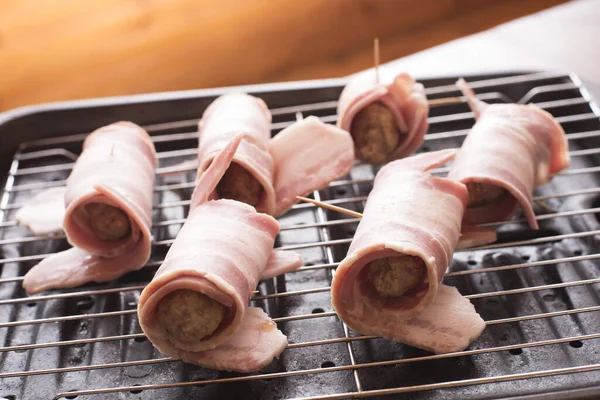 Preparing pigs in blankets on a wire rack with cured ham around pork sausages waiting to be grilled or oven baked