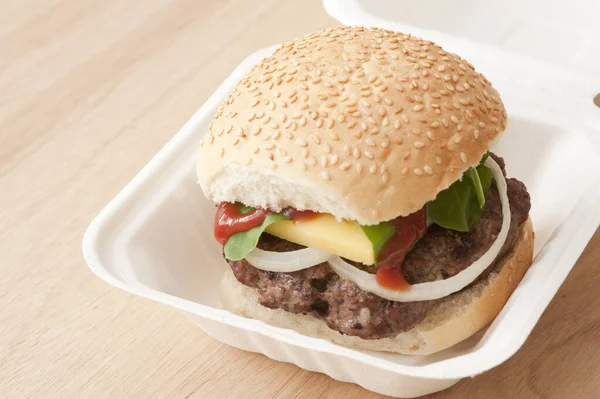 Hamburger takeaway in a disposable container with a thick juicy beef patty, salad trimmings and a slice of cheese