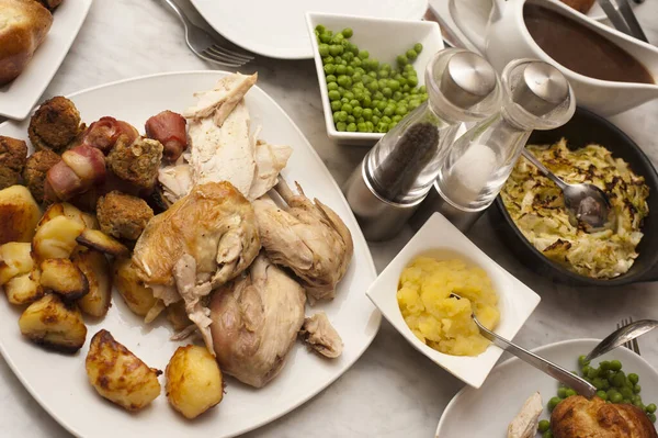 Delicious roast dinner laid out on the table with carved roast chicken or turkey with roast potatoes and accompanying vegetables in individual dishes