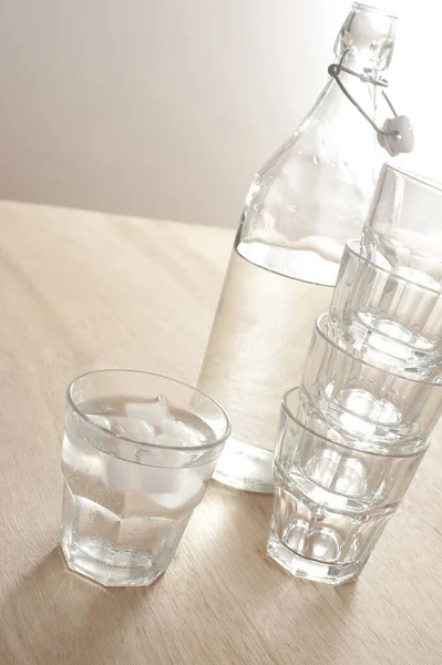 A glass bottle with still water and tumblers on a wooden table