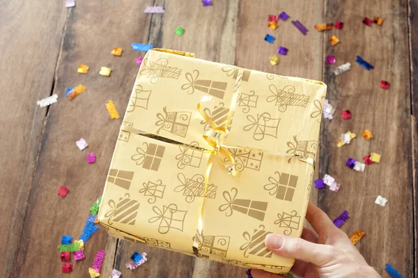 Overhead view of the hand of a man giving a birthday gift in pretty gift wrap over a wooden table background with scattered Happy Birthday sprinkles or confetti
