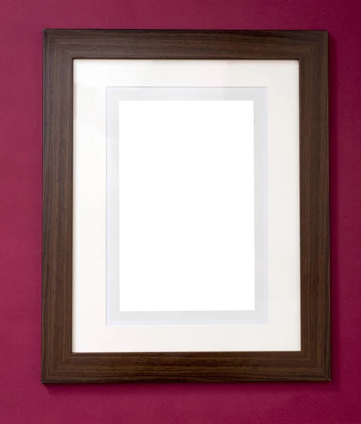 Plain blank wooden picture frame with a black stained border and central white copy space hanging on a burgundy colored wall