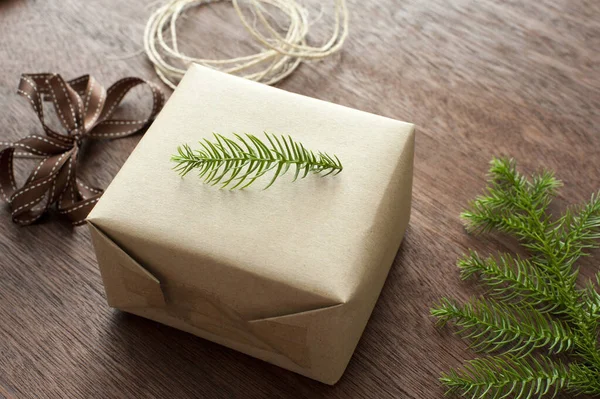 Traditional Christmas gift wrap with a small twig of fresh green pine placed on top of a wrapped gift surrounded by twine, ribbon and a pine branch