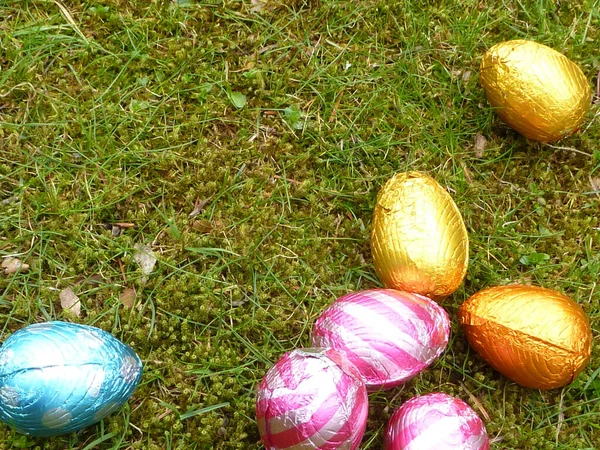 Easter egg hunt background with copy space. Chocolate eggs in colorful foil sitting on fresh grass in the spring