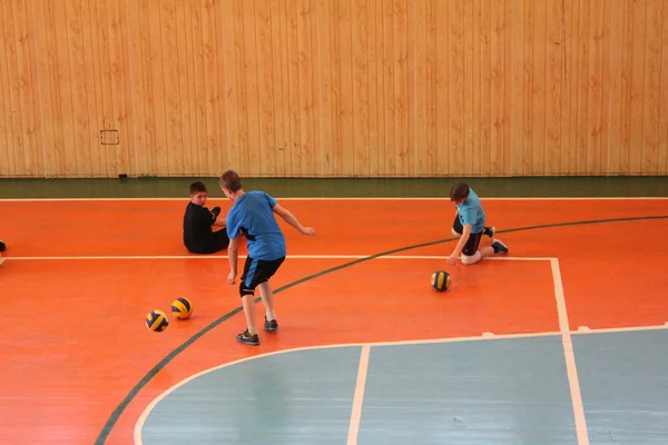 Трое молодых спортсменов играют в мяч на сине-оранжевом поле спортзала — стоковое фото