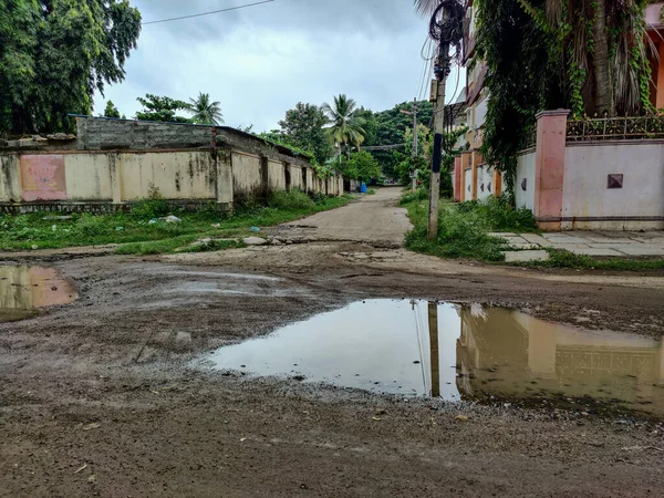 曇りの気候でインド風の家に囲まれたセメントから構築灰色の色の道路のストック写真 大雨の後 雨の水は道路をカバーした 劇的な暗い雲が空を覆いました — ストック写真