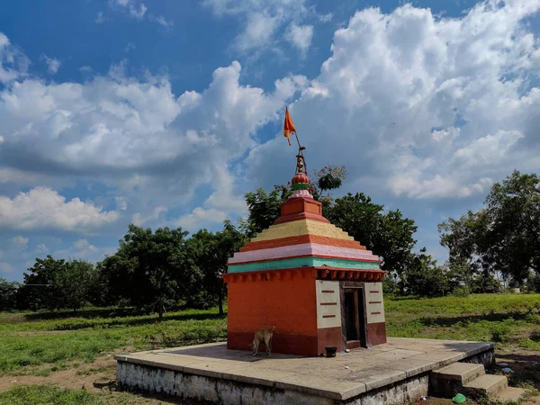 緑の木々 背景に白い雲と青空に囲まれた芝生の土地の真ん中に位置し オレンジの色で描かれたストックフォト小さな古いHindu寺 ガルバーガで撮影された写真 — ストック写真