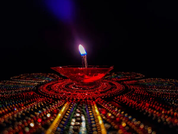 Özellikle Diwali Festivali sırasında koyu arkaplan altında renkli Rangoli 'de tutulan güzel kırmızı plastik lambanın stok fotoğrafı. Fotoğraf Banglore, Karnataka, Hindistan 'da çekildi. lambaya odaklan