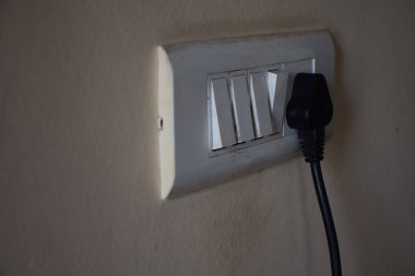 Kolhapur, Maharashtra, Hindistan 'daki açık sarı renkli duvarda siyah dizüstü bilgisayara bağlı beyaz renkli elektrik düğmesi panosunun resmi. nesneye odaklan.