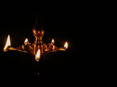 Stock photo of traditional oil lamp made up by brass metal called samai or samayee,it has been lit daily at Indian house for worshiping god . Picture captured under dark background at Bangalore, India clipart