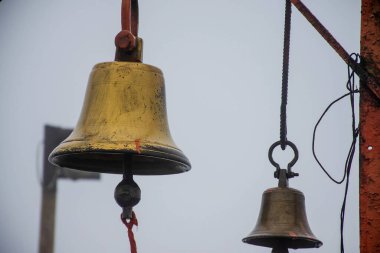Hindu tapınağındaki bulanık arka planda turuncu renkli demir bir çerçeveye asılı iki eski bakır ya da bronz çanın stok fotoğrafı. Fotoğraf Sateri Hill İstasyonu Kolhapur, Maharashtra, Hindistan 'da çekildi..