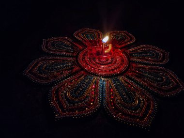 Özellikle Diwali Festivali sırasında koyu arkaplan altında renkli Rangoli 'de tutulan güzel kırmızı plastik lambanın stok fotoğrafı. Fotoğraf Bangalore, Karnataka, Hindistan 'da çekildi. lambaya odaklan