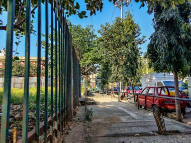 Bangalore, India- 19 Aralık 2021; Yeşil ağaçlarla çevrili kentteki stok fotoğraf boş patikası, patikanın yakınına park edilmiş eski araçlar, Hindistan Bangalore 'da parlak güneş ışığı altında çekilmiş resim.