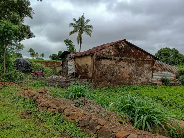 Stock photo of old, damaged red brick house with pyramid shape roof top in the middle of the beautiful farmland. small shelter mad up by roof sheet in the backside of the house at Kolhapur,Maharashtra