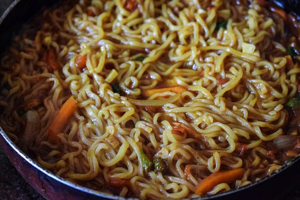 Lezzetli ev yapımı sıcak ve baharatlı erişteler, sebzeler, baharatlar ve kızartma tavasında saklanmış otlar. Resim Hindistan, Karnataka, Bangalore 'da doğal ışık altında çekildi. nesneye odaklan.