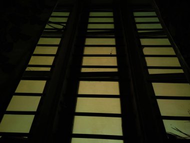 Dikdörtgen şekilli pencerenin, oturma odasında ızgara ve çiçek perdeleri olan resmi. Resim Bangalore, Karnataka, Hindistan 'da karanlıkta çekildi. seçici odak.