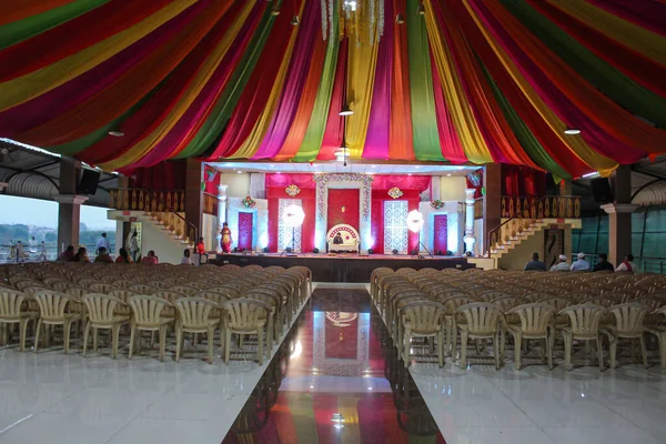 カラフルなカーテンで美しく装飾された結婚式場の屋上やテントのストックフォト 赤バラと明るいライトで飾られたステージ プラスチック製の椅子がステージの前に置かれていました インド式結婚式 — ストック写真
