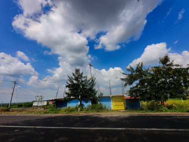 Gulbarga, Hindistan - 6 Ekim 2021; Hindistan 'ın kırsal kesimindeki yol kenarı kapatma dönemi boyunca kapalı. yeşil ağaçlar ve dükkanların yakınındaki boş manzara, arka planda mavi gökyüzü.