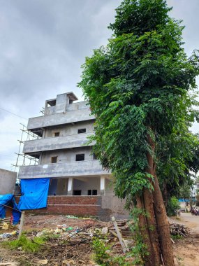 Hyderabad, India- August 6th 2022; Side view of newly build apartment building in the residential area, construction work is on going .Indian lilac or neem tree near the building, clouds on background
