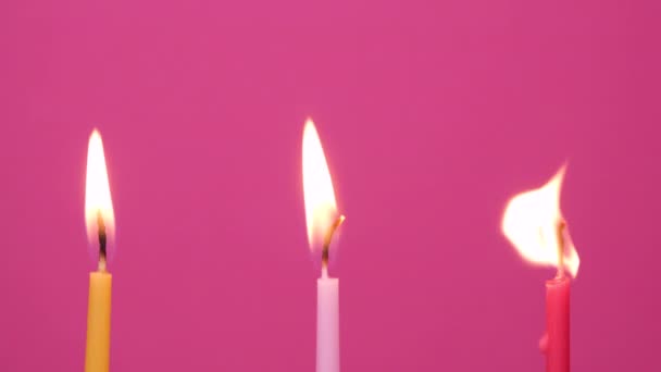 Apagando tres velas de pastel ardiendo sobre un fondo rosado. Cerca de amarillo, rosa y magenta velas de pastel. Vídeo de resolución 4K — Vídeos de Stock