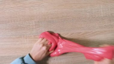 Çamurla oynamak, eğlence ve stres atmak için yapışkan maddeyi germek. Yaklaş ve üst görüntüde kırmızı, parlak balçık tutan ve sıkan kadın elini gör. 4K çözünürlük videosu