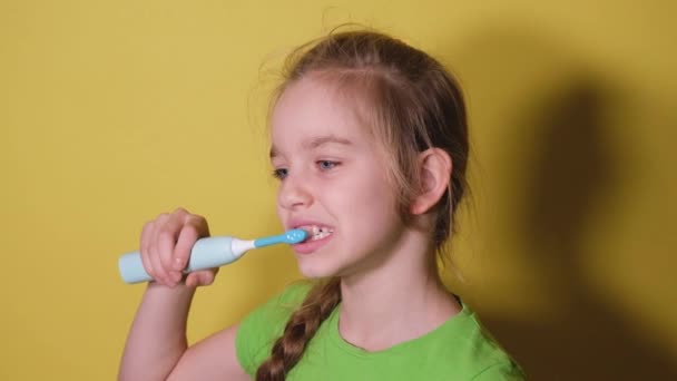 Подросток чистит зубы изолированно на ярко-желтом фоне. Девочка в зеленой футболке пользуется электрической зубной щеткой, чтобы почистить зубы. — стоковое видео