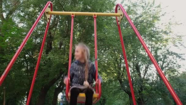 走近快乐和微笑的少女骑着秋千。在公园的木制秋千上玩得很开心的女孩.休闲活动和童年的概念。4k分辨率视频 — 图库视频影像