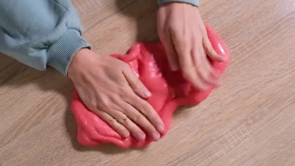 Playing with slime, stretching the gooey substance for fun and stress relief. Close up and top view of female hand holding red shining slime and squeezing it. Full HD slow motion video — Stock Video