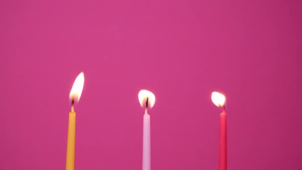 Tre tårtljus brinner på en rosa bakgrund. Närbild på gula, rosa och magenta tårtljus. 4K-upplösning video — Stockvideo