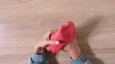 Çamurla oynamak, eğlence ve stres atmak için yapışkan maddeyi germek. Yaklaş ve üst görüntüde kırmızı, parlak balçık tutan ve sıkan kadın elini gör. 4K çözünürlük videosu